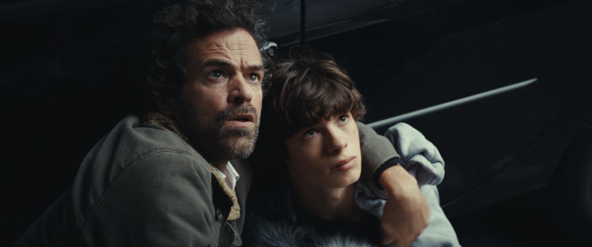 Romain Duris holds Paul Kircher as they look up in fear and lean against a car in The Animal Kingdom